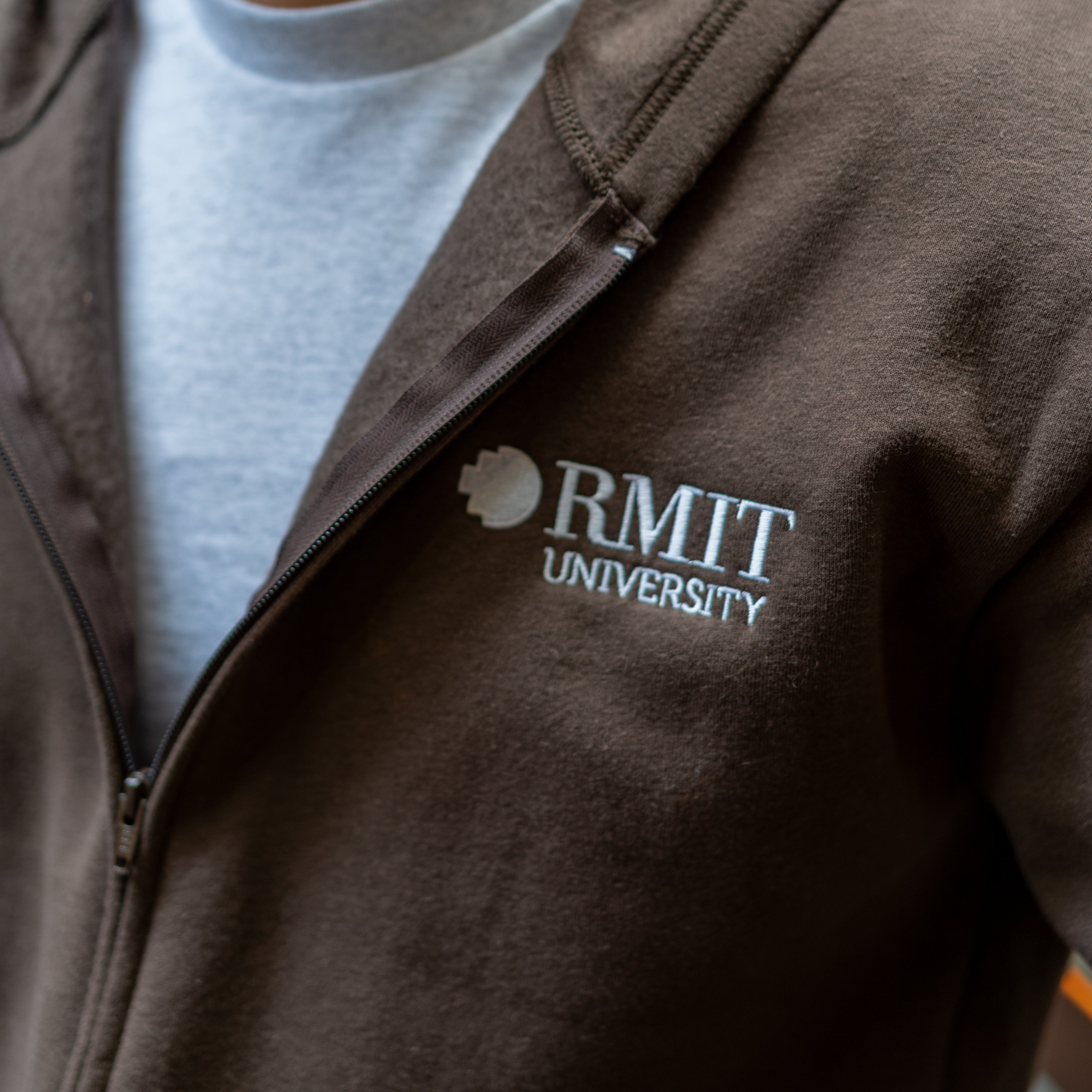 Close-up of RMIT University zip jacket in chocolate brown with white embroidered RMIT logo on chest.