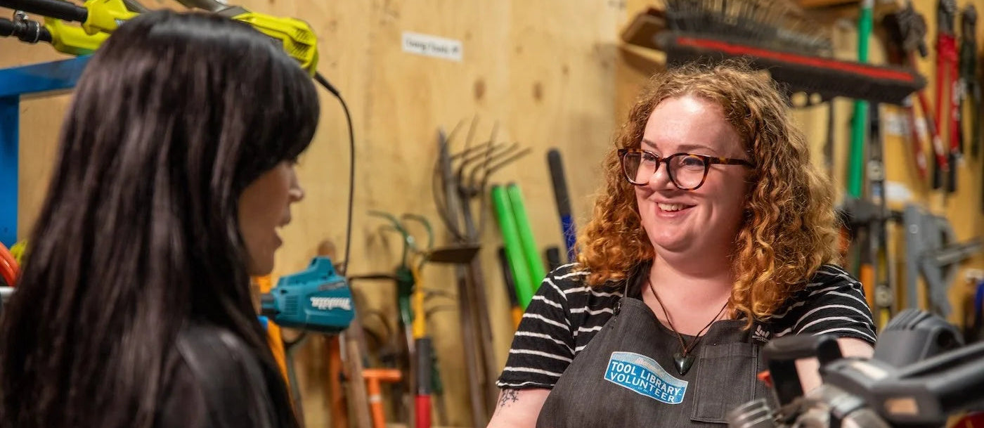 Two women in a workshop setting with tools and equipment in the background